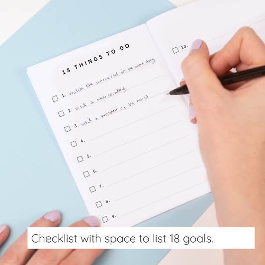Hand holding a pen over a checklist with space to list 18 goals on a light blue background.