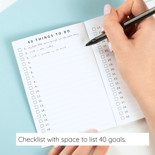 Hand holding a pen over a checklist with space to list 40 goals on a light blue background.